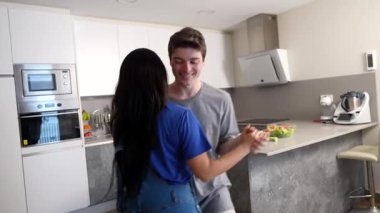 Çok ırklı eşler, mutfak adası yakınlarında neşeli dans anlarını paylaşıyor, spontane hareketler ve paylaşılan mutlulukla neşe ve bağlantılarını ifade ediyorlar.