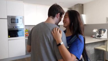 Genç, çok ırklı çift samimi dans ediyor, neşeli bağları paylaşıyor ve modern mutfak ortamında ritmik bir şekilde ilerliyorlar.