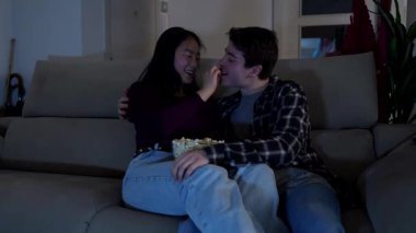 Çok ırklı bir çift patlamış mısır paylaşıyor, rahat bir film gecesinde kanepede yan yana oturuyor, sevgi dolu bir bağ ve samimi bir ev rahatlığı sergiliyor.