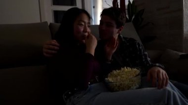 Çok ırklı bir çift evde rahatlatıcı bir akşamın tadını çıkarıyor, patlamış mısır paylaşıyor ve televizyonda bir şeyler seyrediyor.