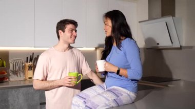Modern mutfaklarında kahve içip sohbet eden çok ırklı genç bir çift hassas ve samimi bir an sergiliyor.