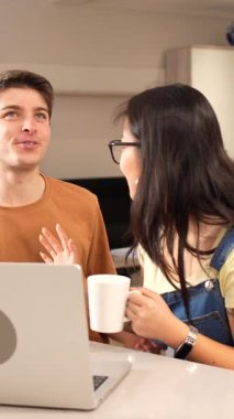 Modern mutfaklarında kahvenin tadını çıkarırken dizüstü bilgisayarda video görüşmesi yapan çok ırklı genç çift.