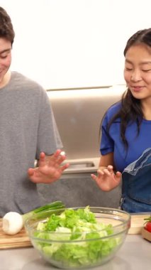 Çok ırklı bir çift birlikte sağlıklı bir yemek hazırlıyor, sebze doğruyor ve mutfaklarında eğleniyorlar.