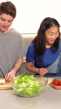 Genç çift modern mutfaklarında birlikte sağlıklı bir salata hazırlıyor, takım çalışması ve aile saadeti sergiliyorlar.