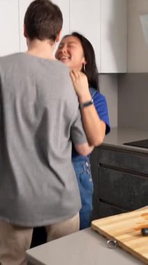 Çok ırklı çift, neşeli hareketler ve paylaşılan mutlulukla neşe ve bağlantılarını ifade ederek, parlak çağdaş mutfakta samimi dans anlarını paylaşıyor.