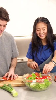 Çok ırklı bir çift birlikte sağlıklı bir salata hazırlıyor, modern mutfaklarında kahkaha ve şefkat paylaşıyorlar.