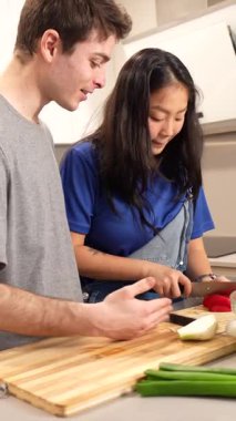 Çok ırklı çift neşe içinde taze, renkli bir salata hazırlıyor. Parlak ev mutfağında yemek pişirme anlarını paylaşıyorlar.