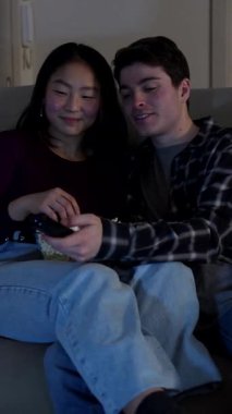 Çok ırklı bir çift, evde rahat bir akşamın tadını çıkarıyor, televizyon izliyor ve bir kase patlamış mısır paylaşıyor.