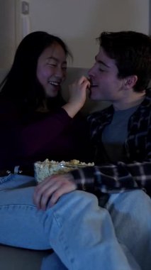 Çok ırklı bir çift, oturma odasındaki kanepelerinde patlamış mısırlarını ve sevgilerini paylaşarak sıcak bir gecenin tadını çıkarıyor.