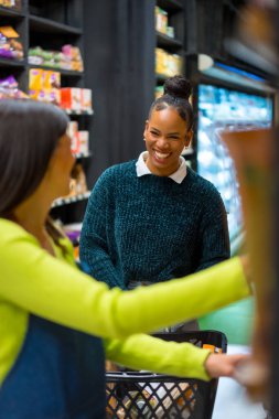 Satıcı kadın, taze sebzelerle dolu canlı bir süpermarkette organik ürünleri seçerken müşteriye yardım ederken gülümsüyor.