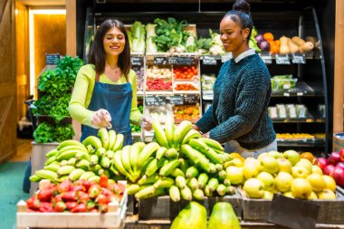 Gülümseyen satıcı kadın organik süpermarkette çeşitli meyve ve sebzelerle taze muz seçiyor.