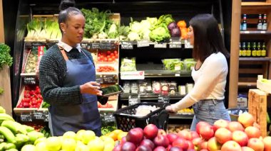 Market çalışanı bir müşteriye tabletle yardım ediyor, süpermarkette taze ürün öneriyor.