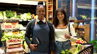 Dost canlısı satıcı ve gülümseyen müşteri organik süpermarket içinde arka planda taze ürün rafları ile pozitif etkileşim paylaşıyor