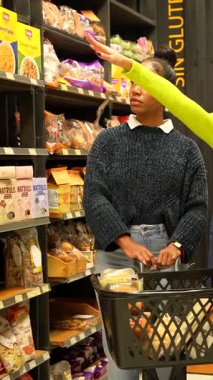 Süpermarket çalışanı bir müşteriye alışveriş sepetiyle yardım ediyor, organik bir mağazada glütensiz ürünler öneriyor.