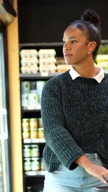 Soğutulmuş raflardan organik bakkaliyeleri dikkatlice seçen, sağlıklı beslenme odaklı mağazalarda sağlıklı besleyici ürünlere göz atan sağlıklı bir kadın.