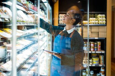 Gülümseyen tezgahtar kadın organik süpermarkette çalışırken dijital tablet kullanarak gıda ürünlerini kontrol ediyor.