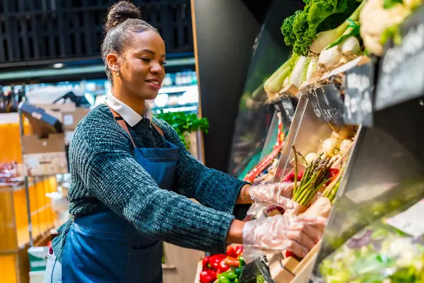 Market çalışanı plastik eldiven takıyor ve süpermarkette taze kuşkonmaz sergiliyor.