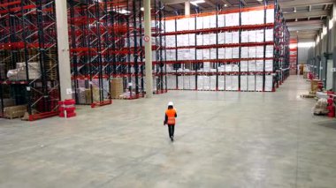 Yüksek görüş açısına sahip güvenlik yeleği giyen profesyonel lojistik danışmanı ve geniş bir depoda güvenli bir şekilde yürüyen, envanter kontrolü yapan ve dağıtım merkezinin operasyonlarını izleyen