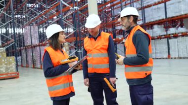 Depo çalışanları barkod tarayıcıları ve panolar kullanarak lojistik ve envanter hakkında tartışıyorlar.