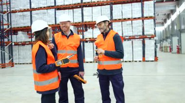 Geniş, organize depolama tesislerindeki envanter yönetim süreçlerini incelerken el bilgisayarı tarama cihazlarını kullanarak, depo lojistik ekibi işbirliği yapıyor.