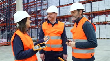 Depo çalışanları, verimli envanter yönetimi için el bilgisayarı kullanarak lojistiği tartışıyorlar.