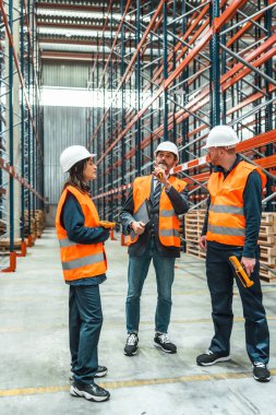 Depo çalışanları ve yöneticileri büyük bir dağıtım merkezinde lojistik operasyonları tartışıyorlar.