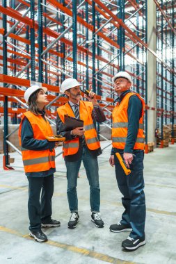Depo çalışanları ve yöneticileri telsiz ve barkod okuyucu kullanarak lojistiği tartışıyorlar.
