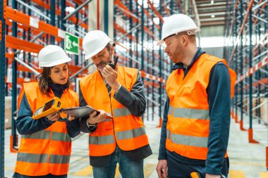 Depo çalışanları envanteri kontrol ediyorlar, barkod tarayıcı ve telsiz kullanıyorlar, büyük bir depoda lojistik ve dağıtım yönetiyorlar.