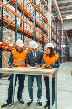 Depo çalışanları ve yönetici toplantısı, büyük bir dağıtım merkezinde barkod tarayıcı ve pano kullanarak lojistik ve envanter tartışması.