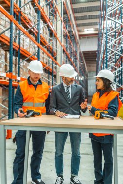 Depo çalışanları ve yönetici lojistiği tartışırken büyük bir dağıtım merkezinde barkod tarayıcıları kullanıyorlar.