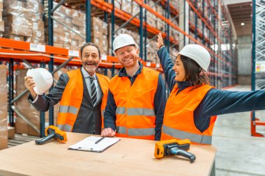 Depo çalışanları ve menajerleri, modern bir depolama tesisinde neşe ve takım çalışmalarını ifade ederek başarılı bir lojistik operasyonu kutluyorlar.