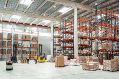 Depo çalışanları lojistiği yönetiyor, forkliftleri çalıştırıyor ve bir dağıtım merkezinde raflardaki paketleri düzenliyorlar.