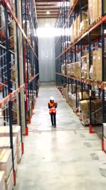 Depo işçisi koridorlarda geziniyor, envanterleri kontrol ediyor ve büyük bir dağıtım merkezindeki lojistiği denetliyor.