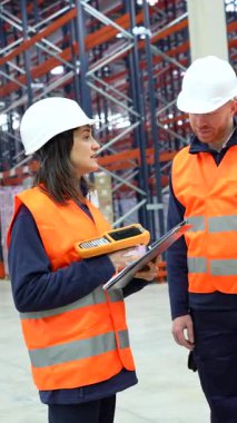 Depo çalışanları barkod tarayıcıları ve panolar kullanarak lojistik ve envanter yönetimini tartışıyorlar.