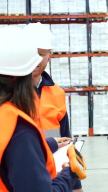 Depo çalışanları envanteri inceliyor ve el bilgisayarı ve pano kullanarak lojistiği tartışıyorlar.