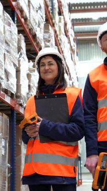 Endüstriyel ortamda verimli lojistik ve envanter yönetimini temsil eden barkod tarayıcı ve pano tutarken depo çalışanları işbirliği yapıyor