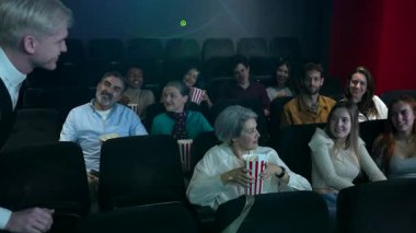 Çeşitli izleyiciler 3D bir filmden zevk alıyorlar, kahkaha ve heyecanla tepki veriyorlar, canlı bir sinema atmosferinde patlamış mısır paylaşıyorlar.