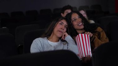 Genç bayan arkadaşlar birlikte rahatlıyor, patlamış mısır paylaşıyor loş aydınlatılmış sinema salonunda film seyrediyor, büyük ekranda hafta sonu eğlencesinin tadını çıkarıyor.