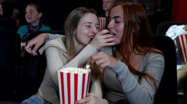 Genç kadınlar patlamış mısır paylaşıyor, loş aydınlatılmış tiyatroda film izlerken birlikte gülüyorlar, akşam eğlencesinde yakın arkadaşlığın tadını çıkarıyorlar.