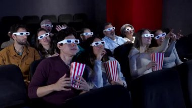 Heyecanlı sinemaseverler 3D gözlük takıyor, patlamış mısır paylaşıyor ve karanlık sinemada büyük ekranda film izlerken coşkulu bir şekilde tepki veriyorlar.