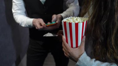 Sinemadaki eğlence deneyimi sırasında elinde patlamış mısır kovası tutan izleyiciler için akıllı telefondan biletleri doğrulayan profesyonel yer gösterici