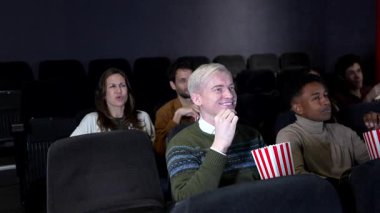 Çok kültürlü genç arkadaşlar karanlık sinema salonundaki 3 boyutlu film gösteriminde kahkahalar atıp patlamış mısır yiyorlar.