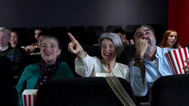 Yaşlı bir çift 3 boyutlu film izliyor, patlamış mısır yiyor ve diğer insanlarla sinemada eğleniyor.