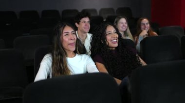 Arkadaşlar, loş aydınlatılmış sinema salonunda eğlenirken kahkaha ve heyecanı paylaşıyorlar. Ortak eğlence anları aracılığıyla gerçek bir bağlantı sergiliyorlar.