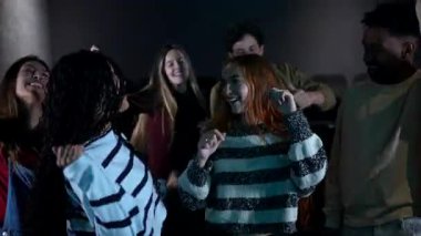 Çeşitli arkadaş grupları coşkuyla dans ediyor, loş ışıklı tiyatroda neşeli anlar paylaşıyor, müzik ve hareketle bağlantıyı kutluyorlar.