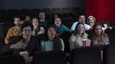 Bir grup insan sinemada heyecanlı bir 3 boyutlu film izlerken tezahürat yapıyor, sarılıyor ve gülüyor, patlamış mısırın tadını çıkarıyor.