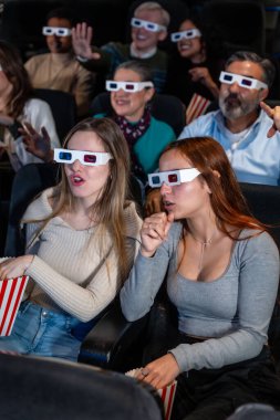 Bir grup farklı arkadaş 3D gözlük takıyor sinemada film seyrediyor, patlamış mısır yiyor ve tepkiler veriyor.