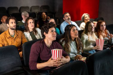 Farklı yaş ve etnik kökenlere sahip insanlar sinemada bir film izliyorlar, ellerinde patlamış mısır kovaları ve gösterinin tadını çıkarıyorlar.