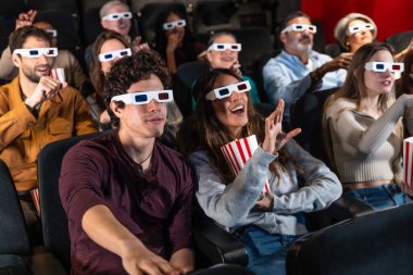 Farklı arkadaş grupları 3D gözlükler takıyor, sinemada film izliyor, patlamış mısır yiyor, birlikte eğleniyorlar.