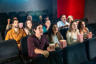 İnsanlar film izleyip sinemada patlamış mısır yiyorlar. Birlikte gösterinin tadını çıkarıyorlar.